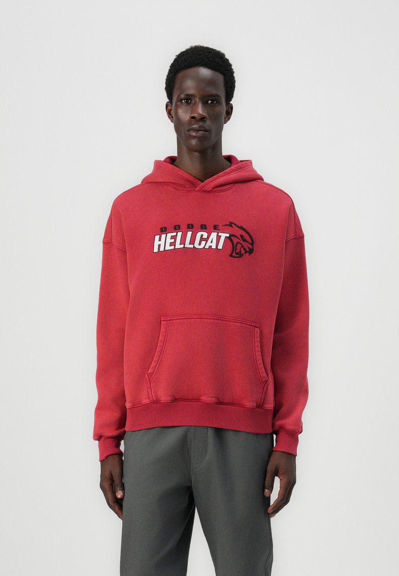Roter Baumwoll-Hoodie mit einer Vorderseitentasche, gerippten Bündchen und Saum sowie dem grafischen Text "DODGE HELLCAT" mit einem Logo. Kombiniert mit grauen Hosen.