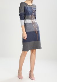 Stickad klänning med horisontella ränder i grått och marinblått, med ett broderat blommönster på ena sidan, långa ärmar och rund halsringning.