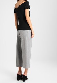 Černý off-shoulder top s krátkými rukávy, v kombinaci se šedými širokými kalhotami a černými sandály na blokovém podpatku. Hladký materiál a volný střih.