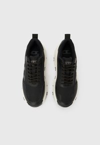 Ανδρικά αθλητικά παπούτσια σε ασπρόμαυρο χρώμα με χοντρή σόλα και σχέδιο με κορδόνια, με επένδυση στο πάνω μέρος, φωτογραφημένα από πάνω σε απλό λευκό φόντο.