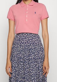 Pink polo shirt with a collared neckline and three buttons, paired with a navy floral print skirt featuring white and pink flowers.