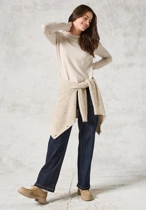 Lichtbeige sweatervet met lange mouwen, gebreide sjaal om de taille geknoopt, donkerblauwe wijde jeans en tan kleurige schoenen. Gladde textuur met een casual ontwerp.