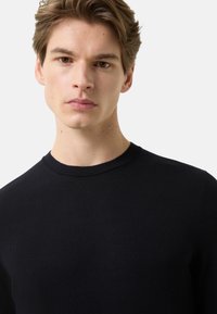 Czarny, dziany sweter z okrągłym dekoltem. Charakteryzuje się gładką strukturą i dopasowanym krojem, prezentując minimalistyczny styl. Brak wyróżniających się wzorów.