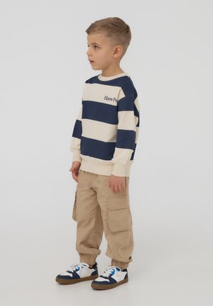 Bambino che indossa una felpa a righe blu navy e crema con la scritta "Divertiti", pantaloni cargo beige e sneaker blu e bianche.