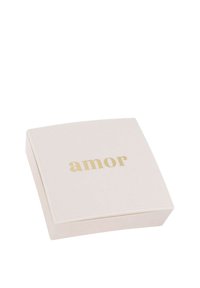 Pequeña caja de joyas cuadrada de color beige claro con la inscripción "amor" en dorado centrada en la tapa contra un fondo blanco.