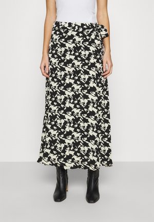 Femme portant une jupe midi à motif abstrait noir et blanc nouée à la taille, associée à des bottes à talons noires.