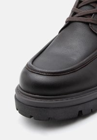 Fekete bőr csizma sima felülettel, kerek orral, vastag gumi talppal, masszív barázdálással, és sötét fűzőkkel. Külső varrási részletek az éleken.