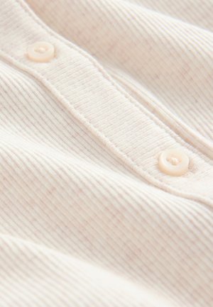 Il tessuto beige chiaro a coste presenta tre bottoni lungo la patta, con una texture morbida e una sottile variazione di colore lungo tutta la superficie.