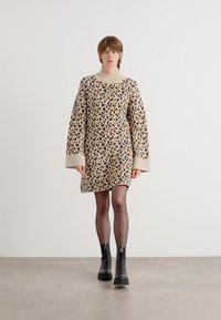 Vestido de malha bege com padrão de leopardo, com um decote amplo e suave e mangas longas e oversized.