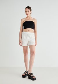 Black strapless top, white shorts with scalloped hem and eyelet details, and black chunky heeled sandals with decorative hardware.