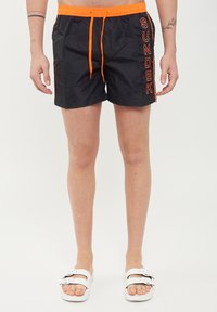 Pantaloni da bagno neri con coulisse arancione e dettaglio del logo "SUNDEK". Realizzati in tessuto morbido, offrono una vestibilità comoda e una lunghezza sopra il ginocchio.