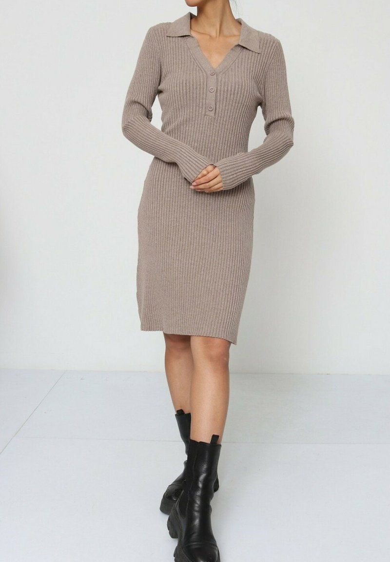 Robe tricotée en brun clair avec une texture côtelée, des manches longues, un décolleté en V et des accents de boutons. Assortie avec des bottines noires à la cheville.