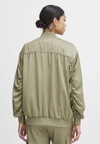 Olivgrön bomberjacka i slät nylon med detaljer i den samlade ärmen och ribbade muddar. Avslappnad passform, med en åtsittande midja.