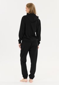 Schwarzes Hoodie- und Sweatpants-Set aus Baumwolle. Verfügt über eine Kapuze, gerippte Bündchen und einen elastischen Bund. Glatte Textur, lockere Passform.