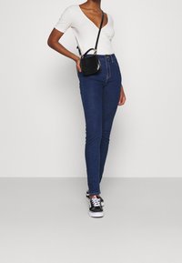 Blå slim fit jeans, vit ribbad t-shirt med v-hals, svart axelremsväska och svarta sneakers med vita sulor. Enkelt design med minimala detaljer.