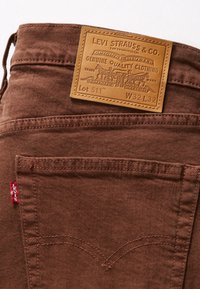 Poche arrière d'un jean Levi's marron avec une étiquette rouge Levi's et un patch en cuir beige indiquant la taille W32 L32 et le style Lot 511.