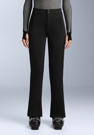 Black flared pants in a stretchy fabric with a smooth texture, featuring a buttoned waist and two zippered pockets on the front.