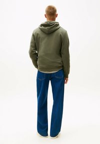 Oliven grøn hoodie med en afslappet pasform, parret med brede blå jeans. Stoffet ser blødt ud, med ribbede manchetter og talje.