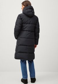 Zwarte pufferjas met een capuchon, met een lange, gewatteerde uitstraling en horizontale panelen. Draag het met blauwe spijkerbroek en zwarte enkellaarsjes.
