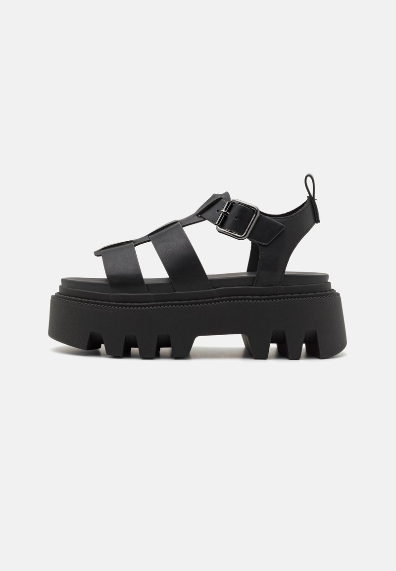 Black platform sandals with thick, ridged soles, featuring multiple strap designs and a side buckle closure for adjustable fit.
