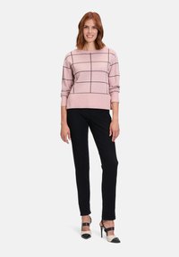 Helles rosa Sweatshirt mit schwarzem Karomuster, rundem Ausschnitt und gerippten Bündchen, kombiniert mit schwarzen, eng anliegenden Hosen und zweifarbigem High-Heels.
