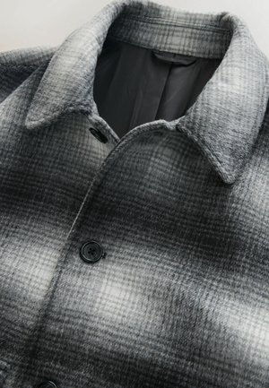 Harmaa ruudullinen takki, jossa on villasekoitekangas, kauluksellinen pääntie ja musta napitus. Sisäosa on vuorattu tasaisella värillä.