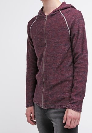 Rode en grijze zip-up hoodie van een gestructureerde stof, met een capuchon en contrasterende stiksels langs de raglanmouwen.