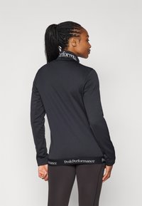 Zwarte langemouwen shirt met een hoge kraag en een logo-band rond de taille. Gladde stof met een getailleerd ontwerp en subtiele stikseldetails.