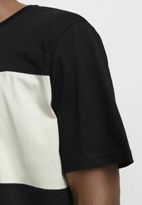 Camiseta a rayas en blanco y negro con cuello redondo. Material de algodón, mangas cortas, textura suave y detalles de costura en contraste.