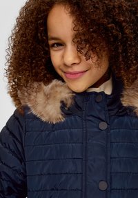 Navy Puffer-Jacke mit horizontalem Steppmuster, ausgestattet mit einem Kunstfellbesatz an der Kapuze, hohem Kragen und schwarzen Druckknöpfen.