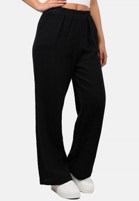 Zwarte wijde-pijpenbroek van een gestructureerde stof, met een elastische tailleband en zijzakken, gecombineerd met witte sneakers.