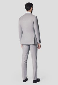Jasnoszary garnitur o dopasowanym kroju, z pojedynczym rozcięciem i czarnymi guzikami. Spodnie mają prosty krój, do zestawione z czarnymi butami.