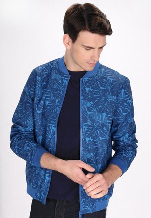 Blaues Bomberjackett mit einem Blattmuster, gerippten Bündchen und einem Reißverschluss. Trägt es über einem marineblauen T-Shirt, das eine glatte Textur und ein leichtes Design aufweist.