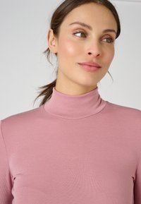 Maglia a collo alto aderente in morbido materiale a coste di un delicato rosa chiaro, caratterizzata da una texture liscia e un design attillato senza decorazioni.