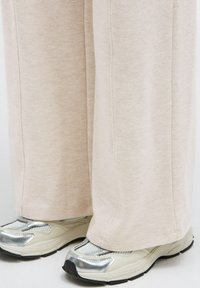 Light beige, ribbed wide-leg pants with a soft texture, paired with chunky sneakers featuring a silver accent and a mesh upper.