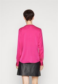 Fuchsia Seidenbluse mit langen Ärmeln, subtiler Glanz, abgerundetem Saum und geknöpften Manschetten, kombiniert mit einem schwarzen Leder-Minirock.