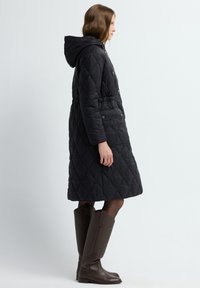 Pikowana czarna kurtka z kapturem, zwężona w talii, z dwoma bocznymi kieszeniami. Połączona z brązowymi wysokimi kozakami do kolan.