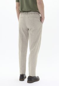Pantaloni beige chiaro con vestibilità rilassata, vita elastica, tasche laterali e tessuto liscio e strutturato. Indossati con scarpe in pelle nere.