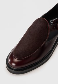 Brown leather slip-on shoe featuring a soft, dark brown fur panel on the upper. Rounded toe with a textured black sole.