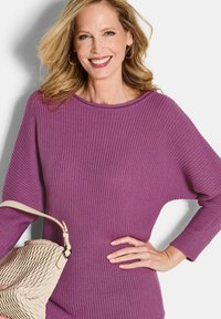 Lila gerippter Strickpullover mit einem lässigen Ausschnitt und langen Ärmeln, kombiniert mit einer cremefarbenen gewebten Handtasche. Glatte Textur, weicher Stoff.