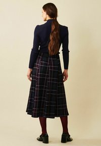 Marinblus med ränder och långa ärmar, kombinerad med en mörk rutig maxikjol med blå och vita linjer, bärs tillsammans med svarta klackskor.