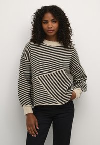 Pull surdimensionné avec des rayures horizontales et diagonales beige et noir, col rond, poignets côtelés et tricot doux et texturé.