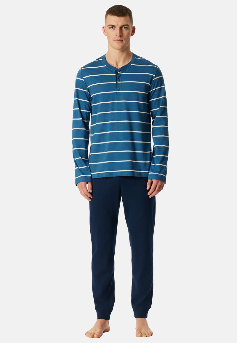 Blaues langärmliges gestreiftes Hemd mit weißen Streifen, mit einem geknöpften Kragen; kombiniert mit marineblauen Jogginghosen. Baumwollstoff.