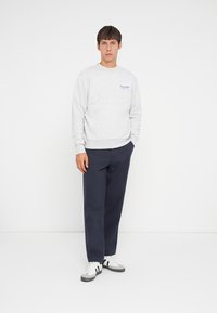 Gray sweatshirt with blue text, ribbed cuffs and hem, paired with navy wide-leg trousers. Footwear features stripes and a white base.