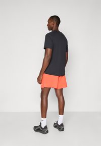 Svart kortärmad T-shirt och klara orange shorts. Sportskor med grå detaljer. Enkel design, slät textur, inga mönster.