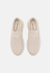 Beige slip-on-sneakers i andningsbar mesh med strukturerad design och vadderad sula för komfort.