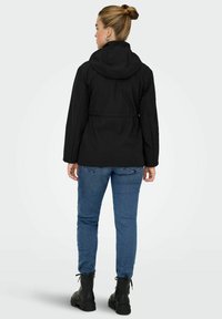 Černá kapucínová bunda s užším pasem, která je spárována s modrými džíny. Mezi významné detaily patří stažený pas a černé vojenské boty.