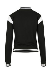 Sweat-shirt noir à coupe cintrée, avec des accents blancs sur les épaules et des poignets et ourlets rayés en blanc et noir. Texture lisse.