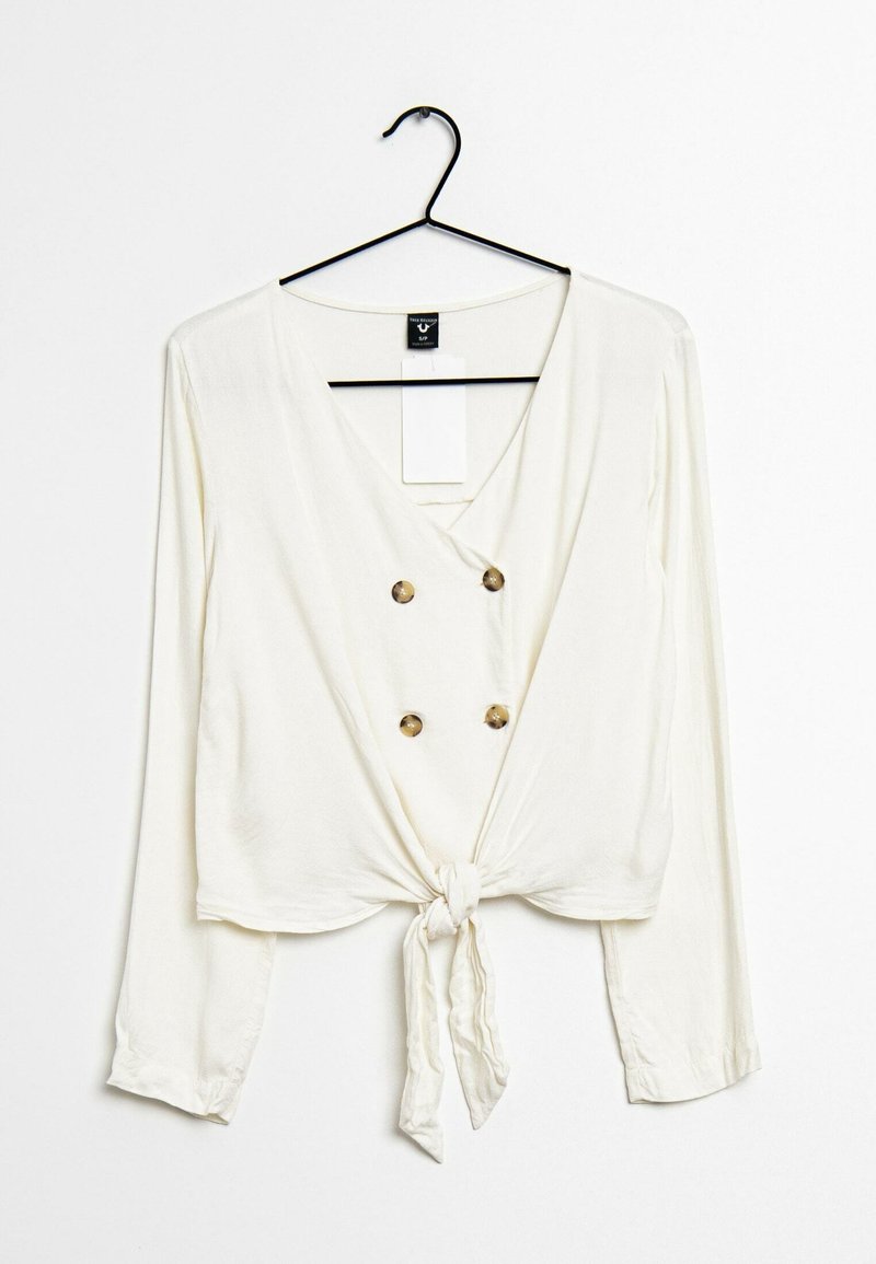 Haut blanc à manches longues avec un col en V, design croisé présentant deux grands boutons dorés, noué à la taille.