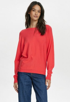 Maglione corallo comodo con scollo a barca e maniche lunghe, abbinato a jeans blu a gamba dritta. Tessuto morbido e design rilassato.